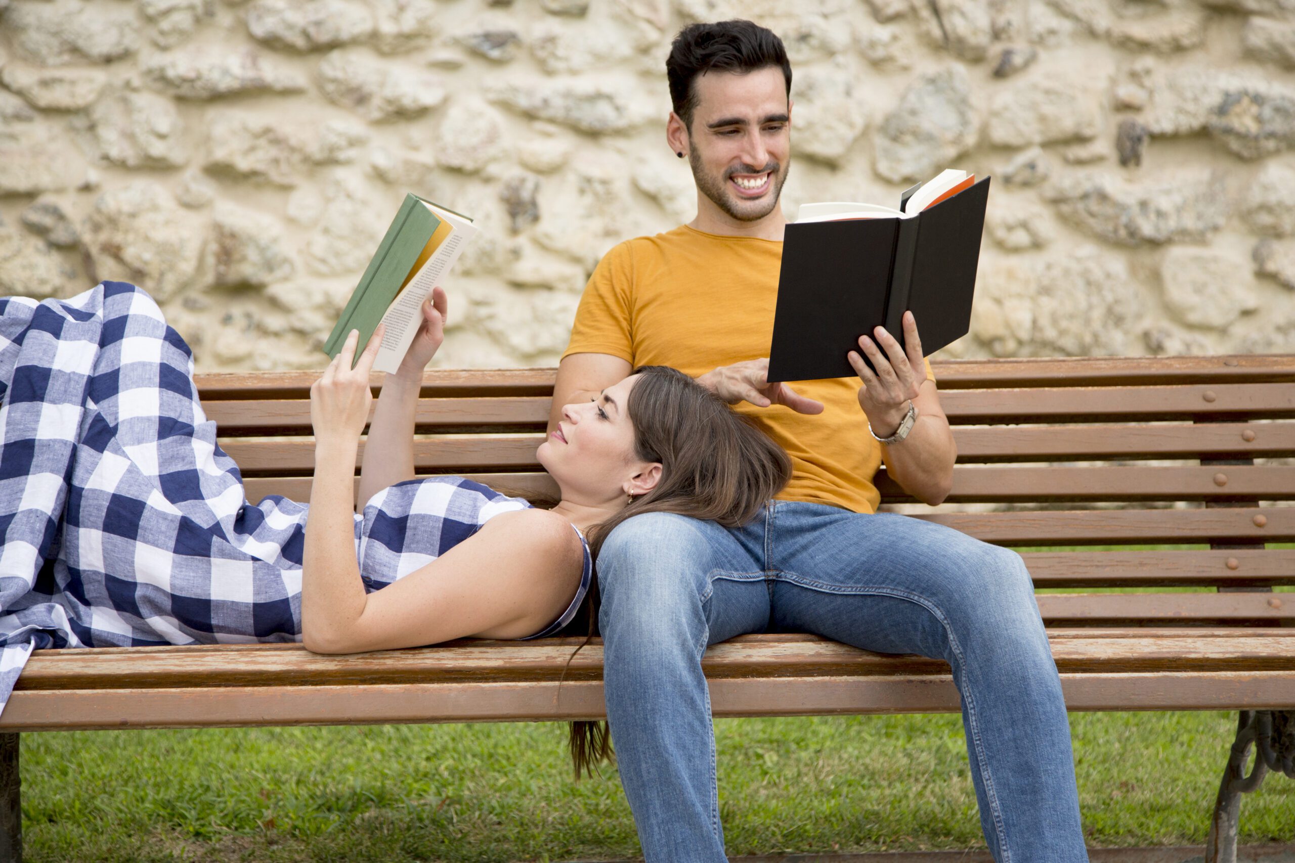 Happy lovers reading books together in a bench of a park